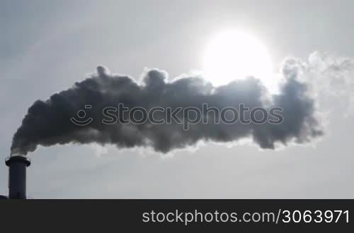 Dicker Qualm oder Rauch aus einem Industrie-Schornstein verdeckt nach und nach die Sonne. Thick steam of an industry chimney hides the sun.