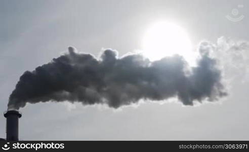 Dicker Qualm oder Rauch aus einem Industrie-Schornstein verdeckt nach und nach die Sonne. Thick steam of an industry chimney hides the sun.