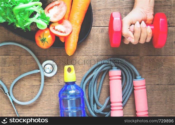 Diet and fitness concept. Woman hand holding dumbbell, healthy foods and fitness equipments on wooden background