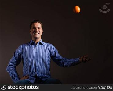 Diet and healthy nutrition. Happy young man throwing orange tropical fruit on dark gray. Studio shot.