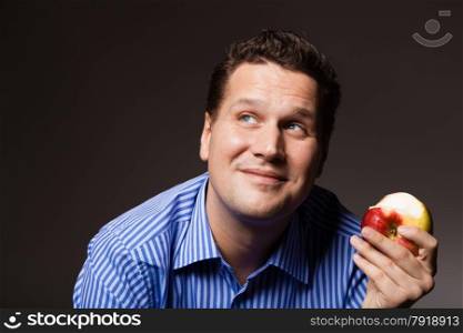 Diet and nutrition. Happy young man eating apple seasonal fruit on dark gray. Guy recommending healthy nutrition.