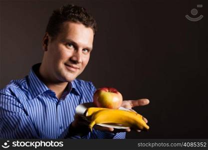 Diet and nutrition. Happy young man holding fruits on dark gray. Guy recommending healthy nutrition.