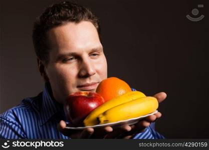 Diet and nutrition. Happy young man smelling fruits on dark gray. Guy recommending healthy nutrition.