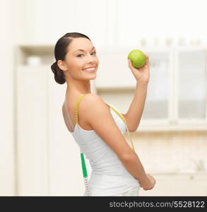 diet and sport concept - beautiful sporty woman with apple and measuring tape in kitchen