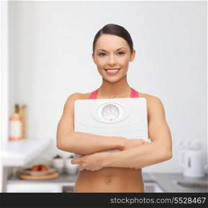 diet and sport concept - beautiful sporty woman with scale in kitchen