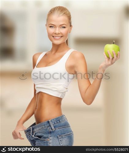 diet and sport concept - sporty woman showing big pants and apple in kitchen