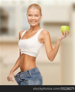 diet and sport concept - sporty woman showing big pants and apple in kitchen