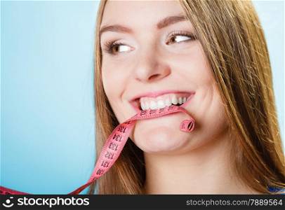 Diet and weight loss concept. Attractive woman holding pink measuring tape between teeth on blue background.