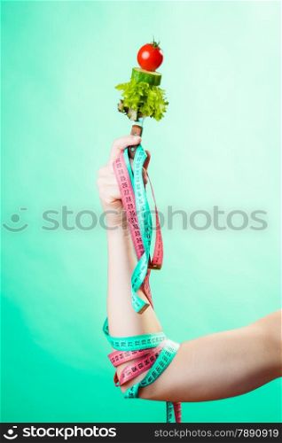 Diet and weight loss concept. Dietician woman hand with vegetarian food and colorful measuring tapes on green blue background.