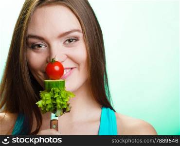 Diet and weight loss concept. Funny girl fitness woman holding fork with fresh mixed vegetables on green blue background.