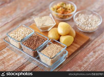 diet, cooking, culinary and carbohydrate food concept - close up of grain, cereals in glass bowls and potatoes on table