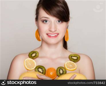 Diet. Girl with necklace and earrings of fresh citrus fruits holding bananas on gray. Woman recommending healthy nutrition.