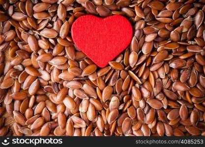 diet healthcare concept. Brown raw flax seeds linseed as natural background and red heart symbol. Healthy food for preventing heart diseases. Flaxseeds are full of omega-3 fatty acids.