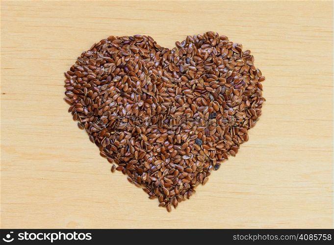 Diet healthcare concept. Raw flax seeds linseed heart shaped on wooden background. Healthy food for preventing heart diseases.