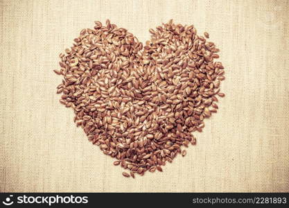 Diet healthcare healthy food. Raw flax seeds linseed heart shaped on sack burlap background.