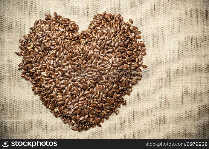 Diet healthcare healthy food. Raw flax seeds linseed heart shaped on sack burlap background.