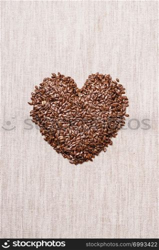 Diet healthcare healthy food. Raw flax seeds linseed heart shaped on sack burlap background.