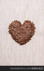 Diet healthcare healthy food. Raw flax seeds linseed heart shaped on sack burlap background.