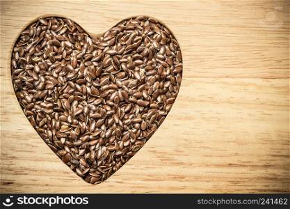 Diet healthcare healthy food. Raw flax seeds linseed heart shaped on wooden board background.