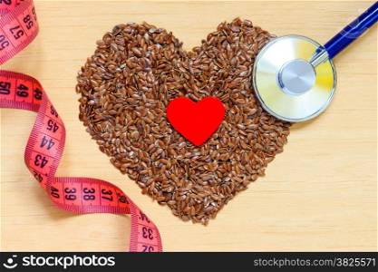 Diet healthcare weight reduction concept. Flax seeds linseed heart shaped stethoscope and measuring tape. Healthy food for preventing heart diseases, overweight.