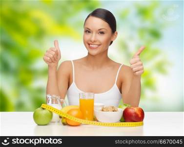 diet, healthy eating and people concept - woman with breakfast and tape measure on table showing thumbs up over green natural background. woman with food and tape measure showing thumbs up. woman with food and tape measure showing thumbs up