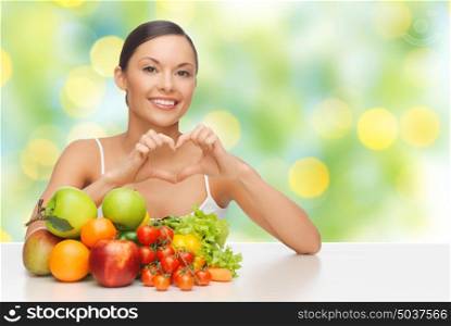 diet, healthy eating, food and people concept - happy woman with lot of fruits and vegetables showing heart over green summer lights background. woman with fruits and vegetables showing heart