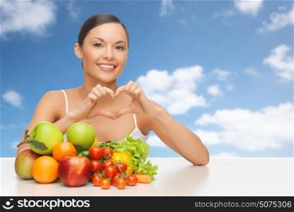 diet, healthy eating, food and people concept - happy woman with lot of fruits and vegetables showing heart over blue sky and clouds background. woman with fruits and vegetables showing heart