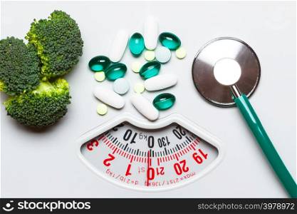 Diet healthy eating weight control and health care concept. Closeup green broccoli stethoscope pills on white scales, choice between