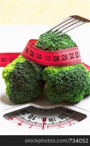 Diet healthy eating weight control concept. Closeup green broccoli measuring tape and fork on white scales