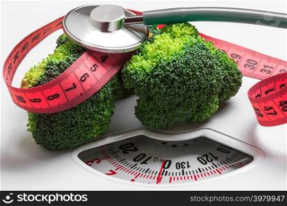 Diet healthy eating weight control concept. Closeup green broccoli with measuring tape and stethoscope on white scales