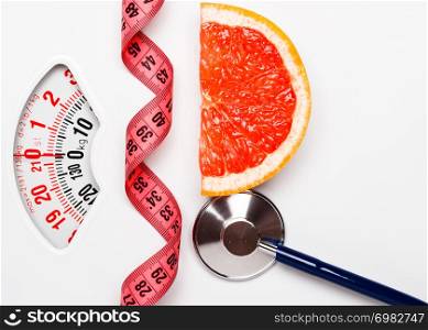 Diet healthy eating weight control concept. Grapefruit with measuring tape and stethoscope on white scales