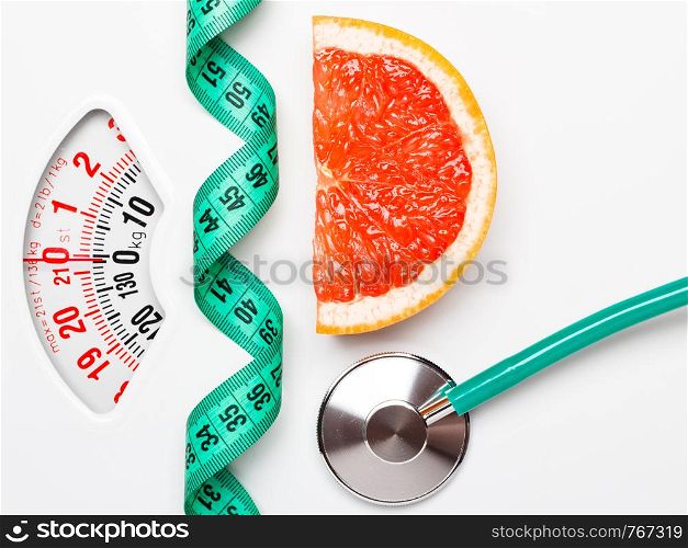 Diet healthy eating weight control concept. Grapefruit with measuring tape and stethoscope on white scales