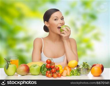 diet, healthy food and people concept - woman eating green apple with vegetables and fruits on table over green natural background. woman eating green apple. woman eating green apple