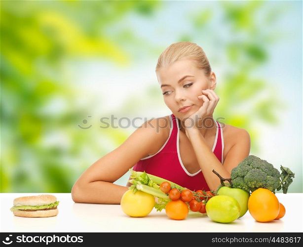 diet, junk food and eating concept - doubting woman with fruits and vegetables looking at hamburger over green natural background. doubting woman with fruits looking at hamburger. doubting woman with fruits looking at hamburger
