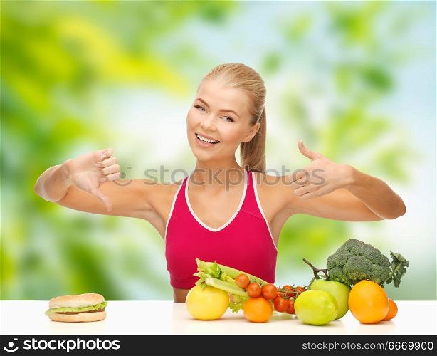 diet, junk food and eating concept - happy smiling woman with vegetables and hamburger showing thumbs up and down sign over green natural background. happy woman with fruits at hamburger. happy woman with fruits at hamburger