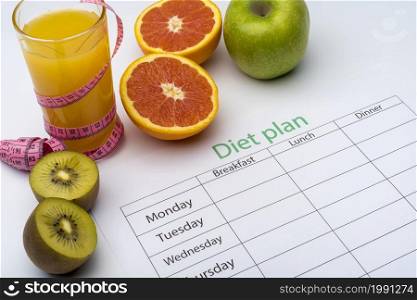Diet plan on a piece of paper, next to a glass of orange juice. Fresh grapefruit, kiwi and Apple with centimeter on white background. The concept of healthy eating.. Diet plan on a piece of paper, next to a glass of orange juice. Fresh grapefruit, kiwi and Apple with centimeter on white background.