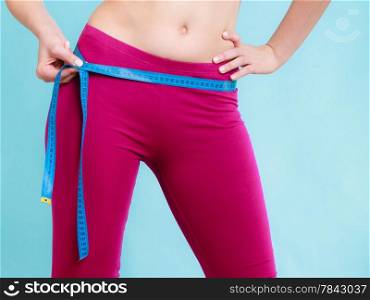 Diet slimming weight loss. Health care and healthy nutrition. Closeup of female body. Fitness woman fit girl with measure tape measuring her loins on blue.