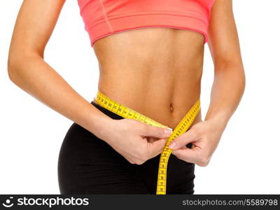 diet, sport, fitness and heath concept - close up of female hands measuring waist with measuring tape