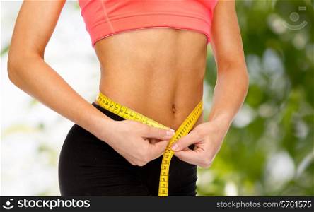 diet, sport, fitness and heath concept - close up of female hands measuring waist with measuring tape