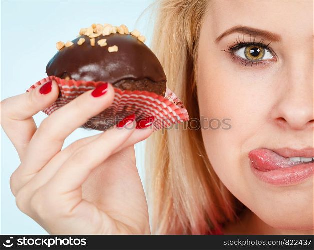 Diet, sweets, food concept. Woman holding delicious chocolate cupcake with peanut frosting about to take bite sticking her tongue out. Woman holding chocolate cupcake about to bite