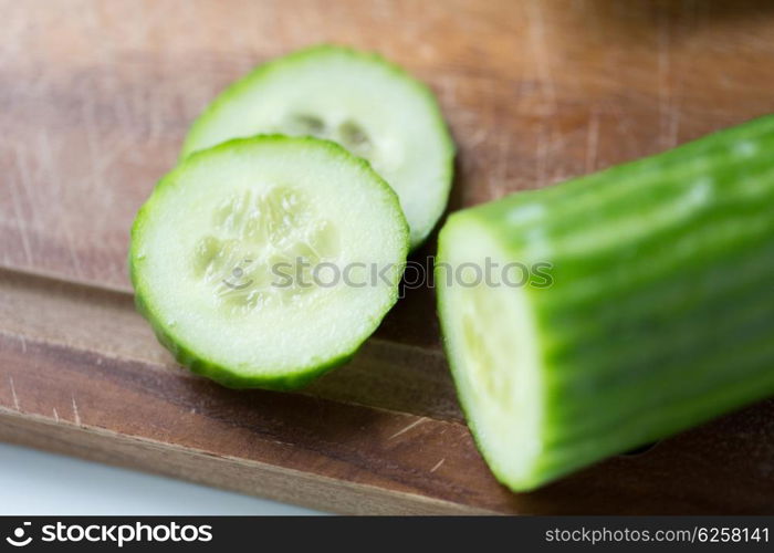 diet, vegetable food, cooking and objects concept - close up of cucumber on wooden cutting board