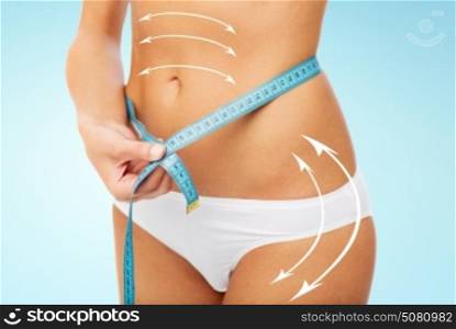 diet, weight loss and people concept - close up of woman body with measure tape around waist over blue background. close up of woman body with measure tape on waist