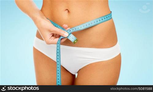 diet, weight loss and people concept - close up of woman body with measure tape around waist over blue background. close up of woman body with measure tape on waist