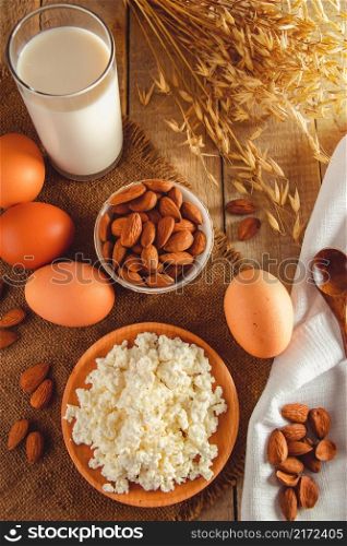 Dietary protein food on wooden background. Rustic breakfast - eggs, cottage cheese and milk on a linen napkin. Vertical photo. Rustic protein balanced diet food. Cottage cheese, eggs, nuts and milk on a wooden background.