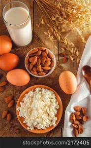 Dietary protein food on wooden background. Rustic breakfast - eggs, cottage cheese and milk on a linen napkin. Vertical photo. Rustic protein balanced diet food. Cottage cheese, eggs, nuts and milk on a wooden background.