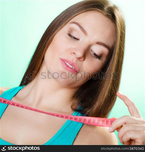 Dieting and weight loss concept. Sporty girl fitness woman holding measuring tape on green-blue background.