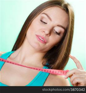 Dieting and weight loss concept. Sporty girl fitness woman holding measuring tape on green-blue background.