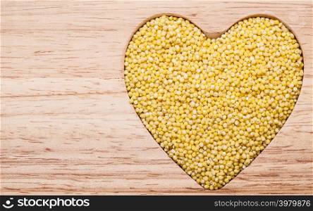 Dieting concept. Millet groats heart shaped on wooden surface. Healthy food help lower cholesterol.