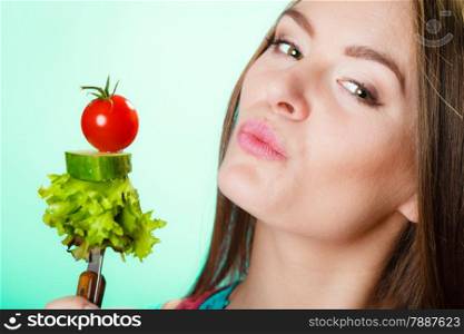 Dieting, healthcare and weight loss concept. Sporty girl fitness woman with measuring tape on neck and holding fork with fresh mixed vegetables on green blue background. Studio shot.