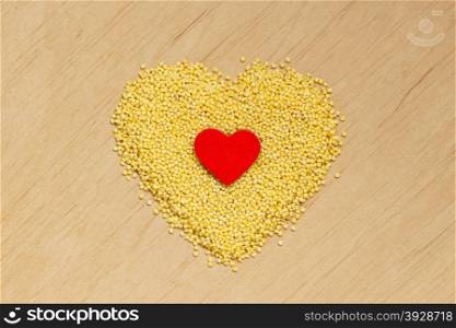 Dieting healthcare concept. Millet groats heart shaped on wooden surface. Healthy food gluten-free and highly alkaline.